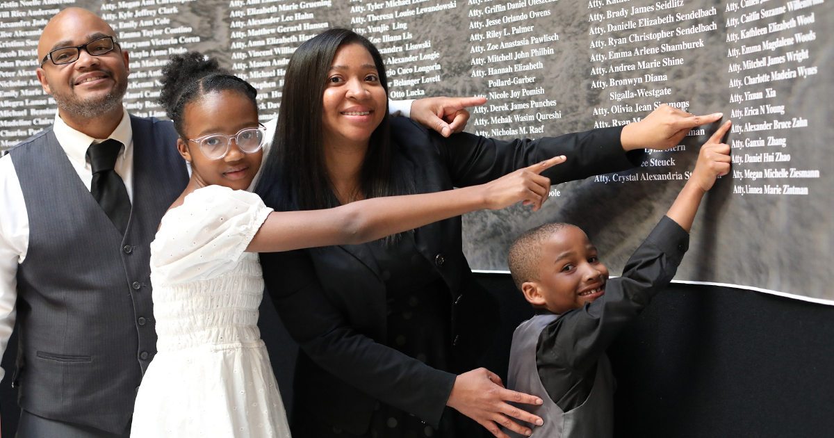 family of four points to the name of a new lawyer on a large sign listing 170 names