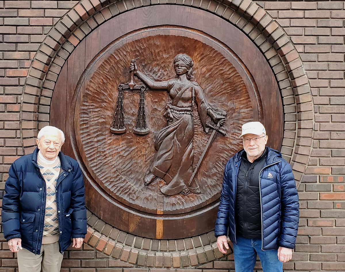 Myron LaRowe (left) and James Gerlach standing next to carving of Lady Justice on the front of LaRowe & Gerlach S.C. on Main Street in downtown Reedsburg, Wis. The medallion now resides at the State Bar Center in Madison.