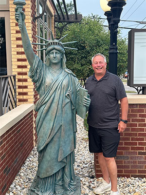Robert Gray smiling and standing next to a small version of the Statue of Liberty