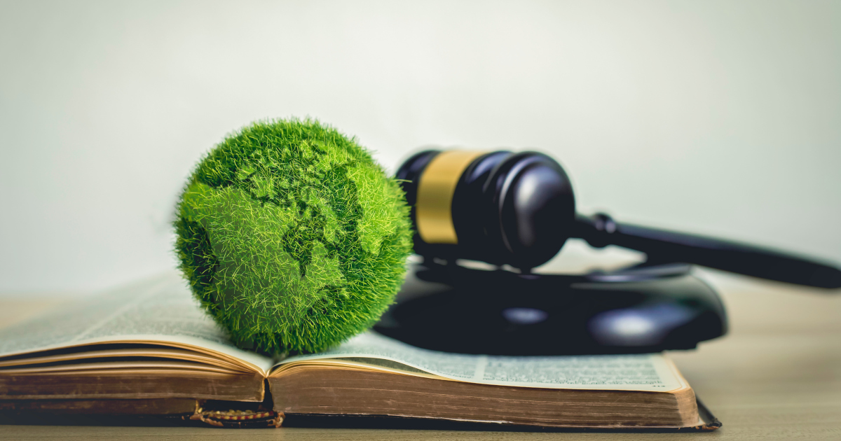 A Green Grass Globe Sitting Atop A Law Book With A Judge's Gavel In The Background