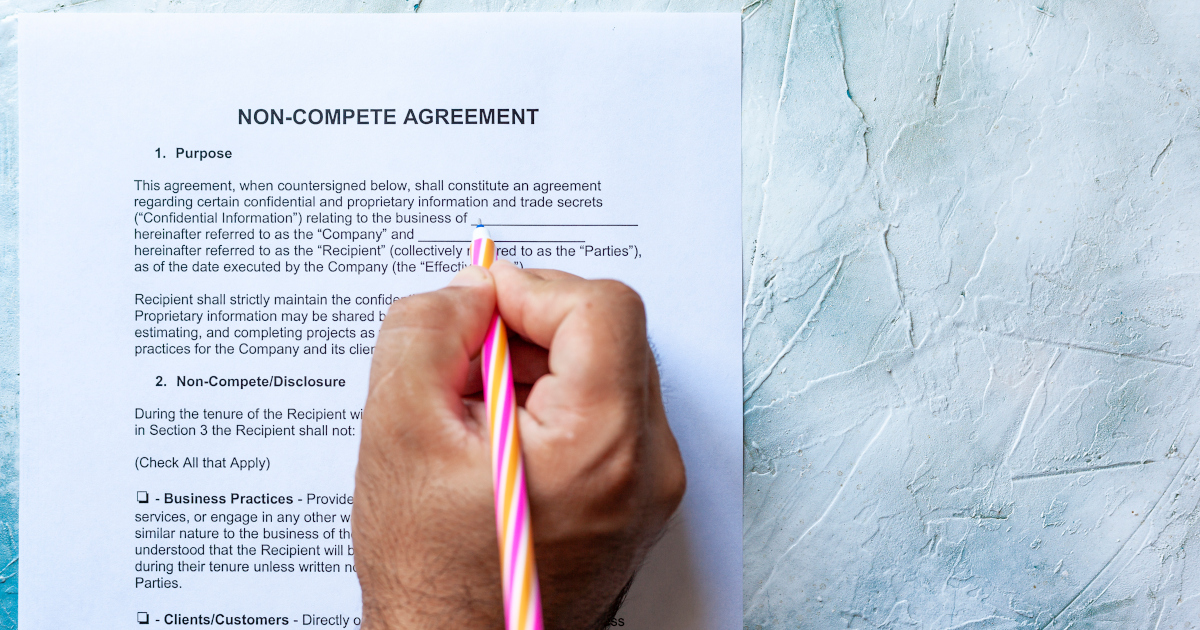 A White Man’s Hand Holding A Pen And Signing A Non-Compete Agreement