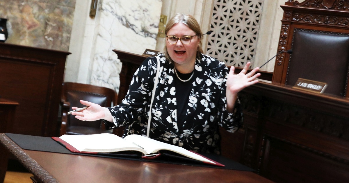 a woman stands with hands raised to celebrate signing the roll book