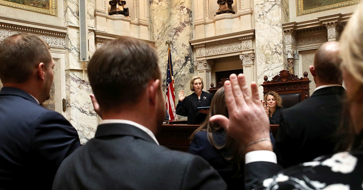 a group of people stand with hands raised as the justice administers the oath