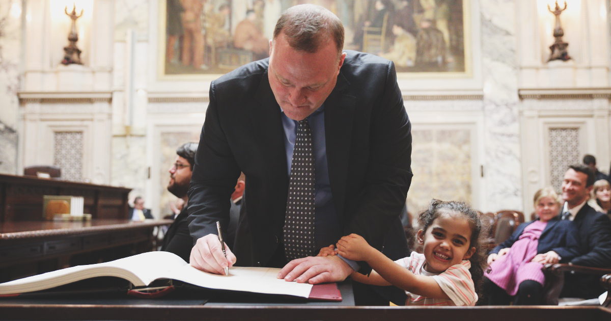 Gregory James Mayew signs the Attorneys Roll book with young daughter holding his arm
