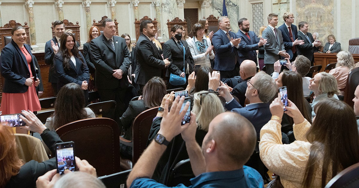 a large group of people standing as a group of seated people applaud and take photos