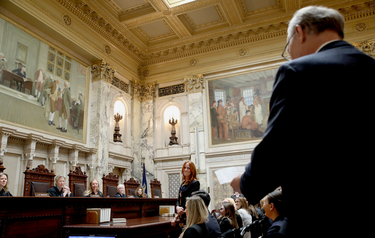 one person standing and reading from a paper as another stands in the Supreme Court Hearing Room
