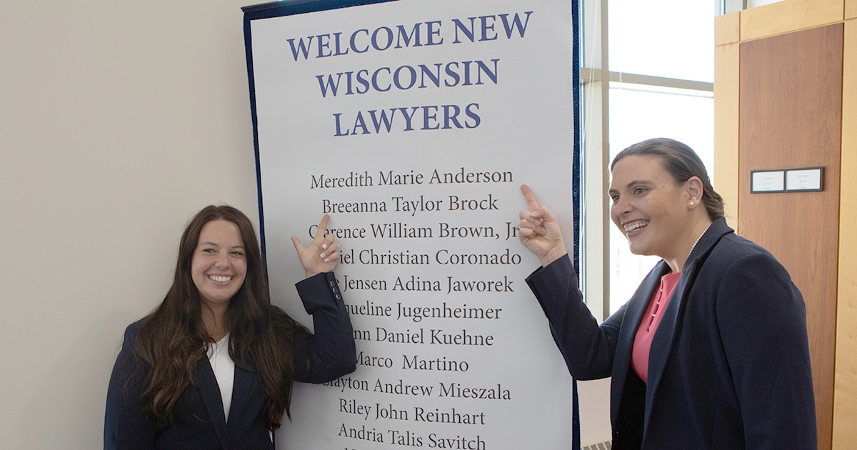 two smiling women pointing to their names on a large list of names