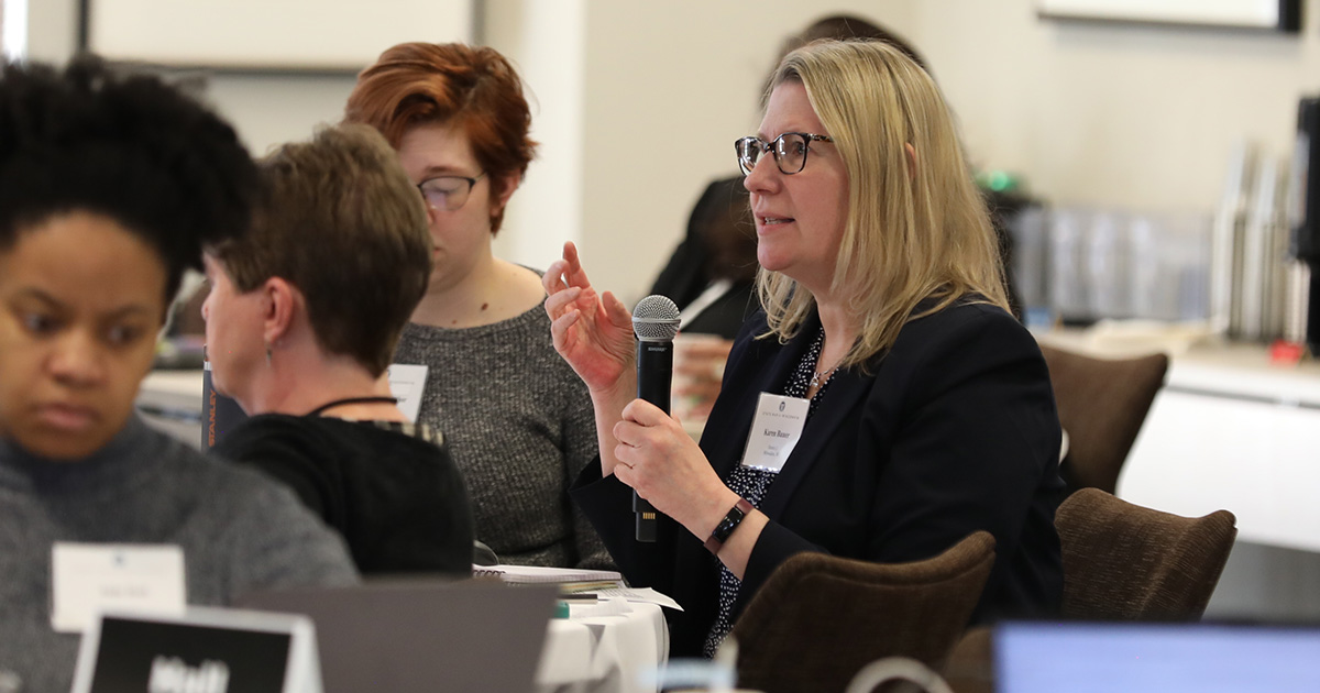 a woman seated at a table and speaking into a microphone