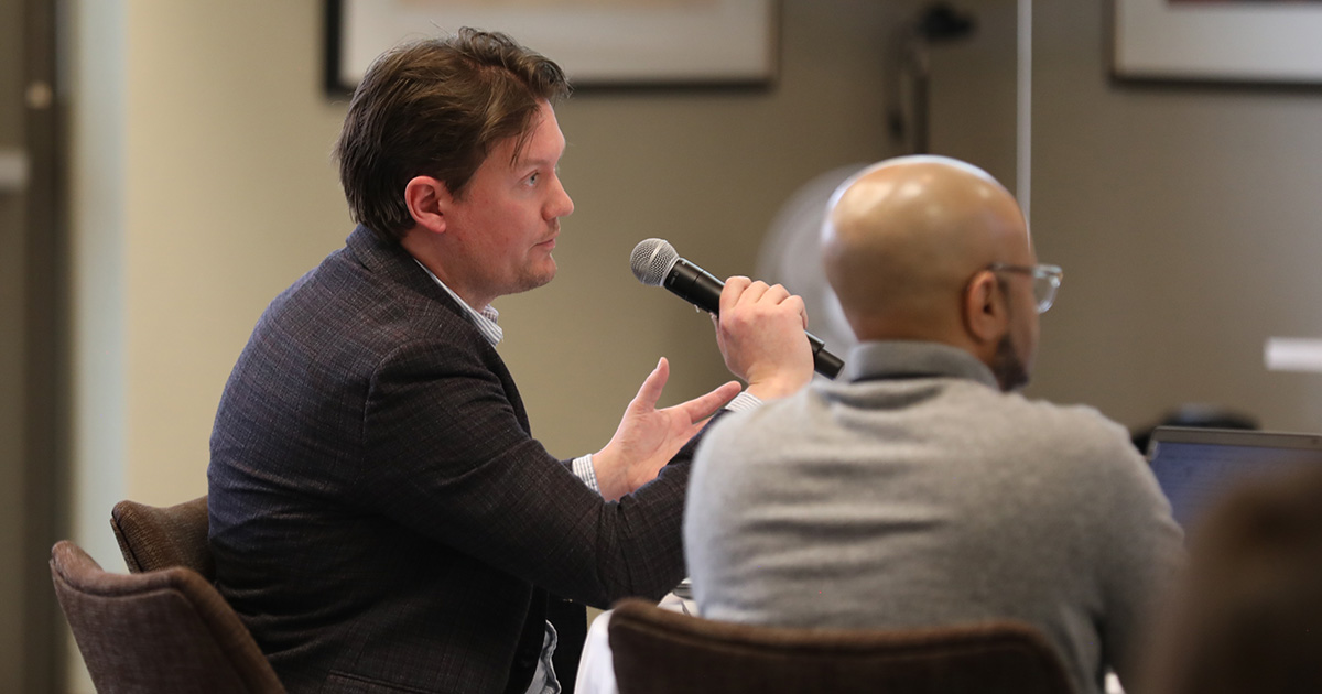 a man seated at a table speaking into a microphone