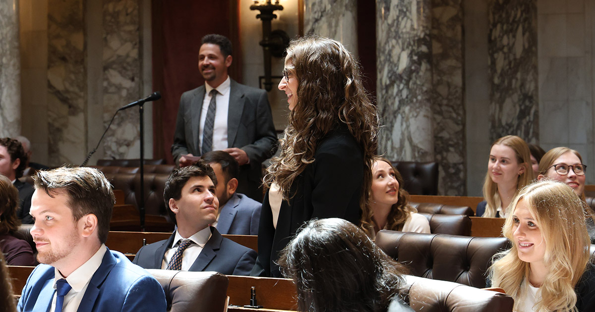 in a room of seated people, two people are standing and smiling