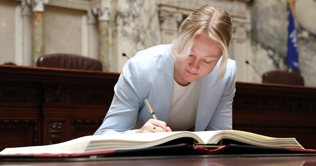 a woman leans over a table, signing a book