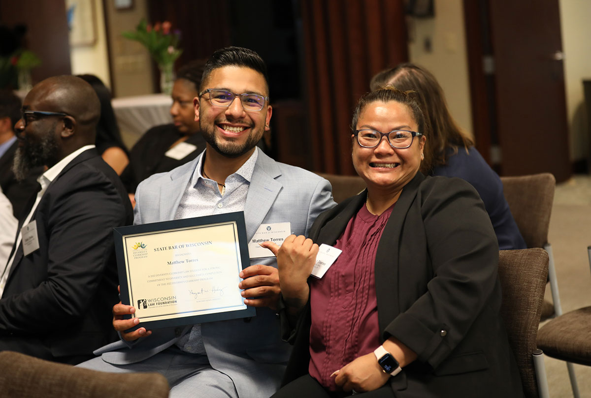 Two participants sit and smile, with the clerk holding his certificate