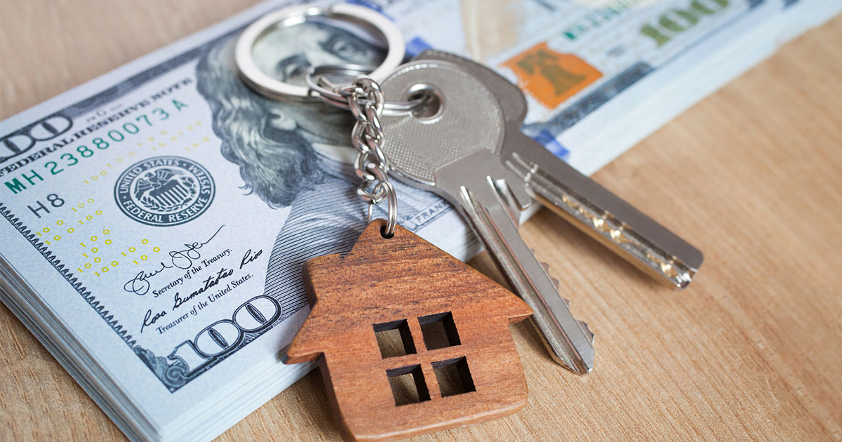 keys with keychain in shape of house on top of stack of money