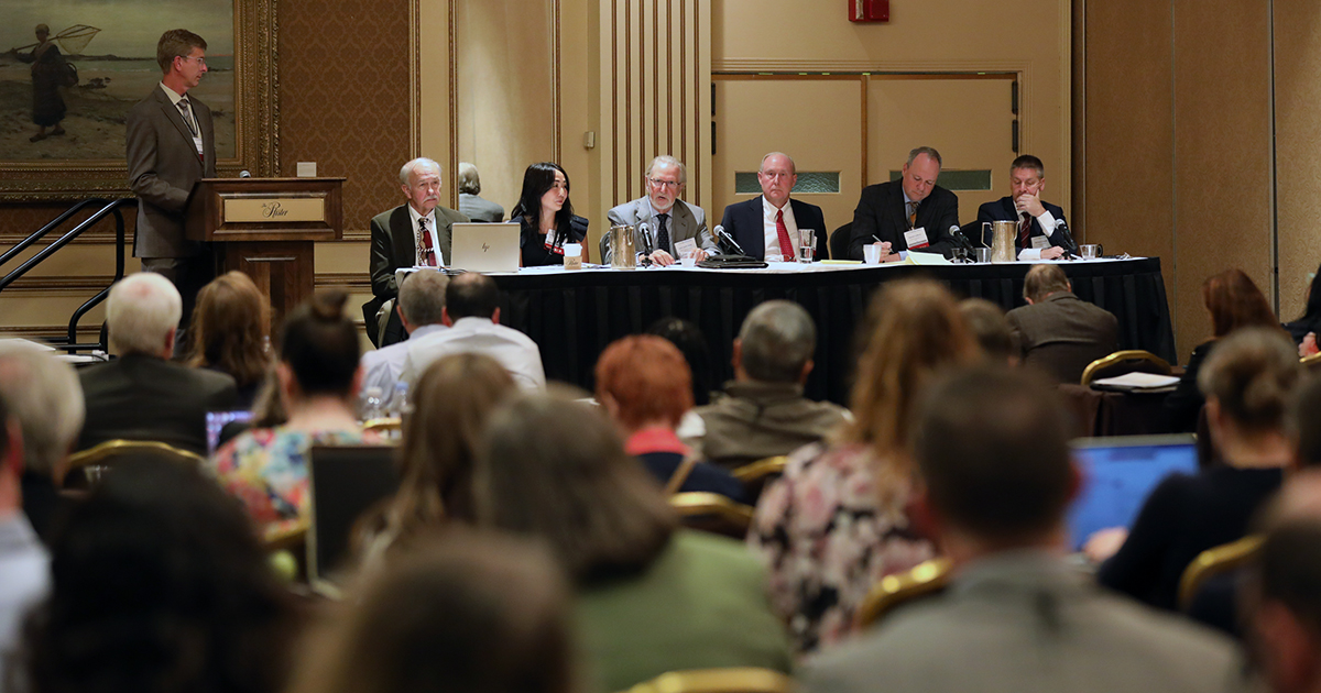 a panel of speakers sit at the front of a seated crowd in a CLE room