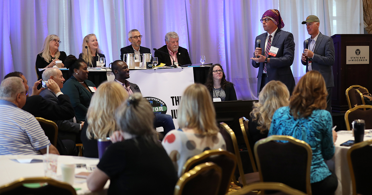 a panel of speakers are at the front of a seated crowd in a large ballroom