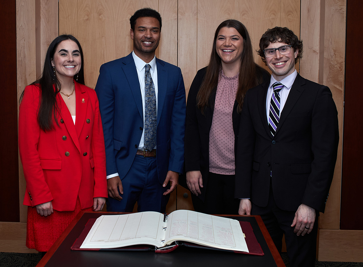 a smiling group of four people standing in front of a large open book on a table