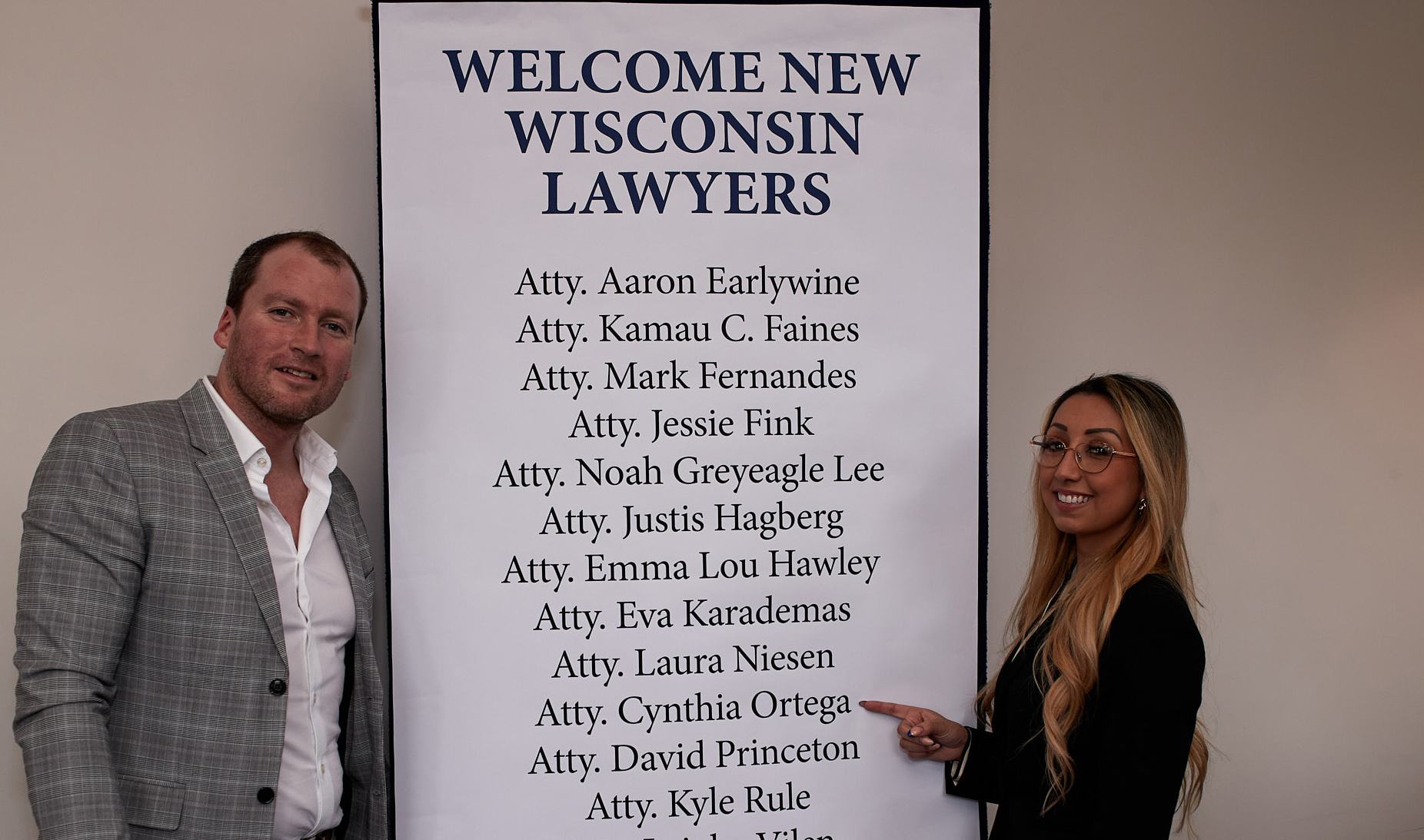 a man and woman stand to each side of a banner with a list of names