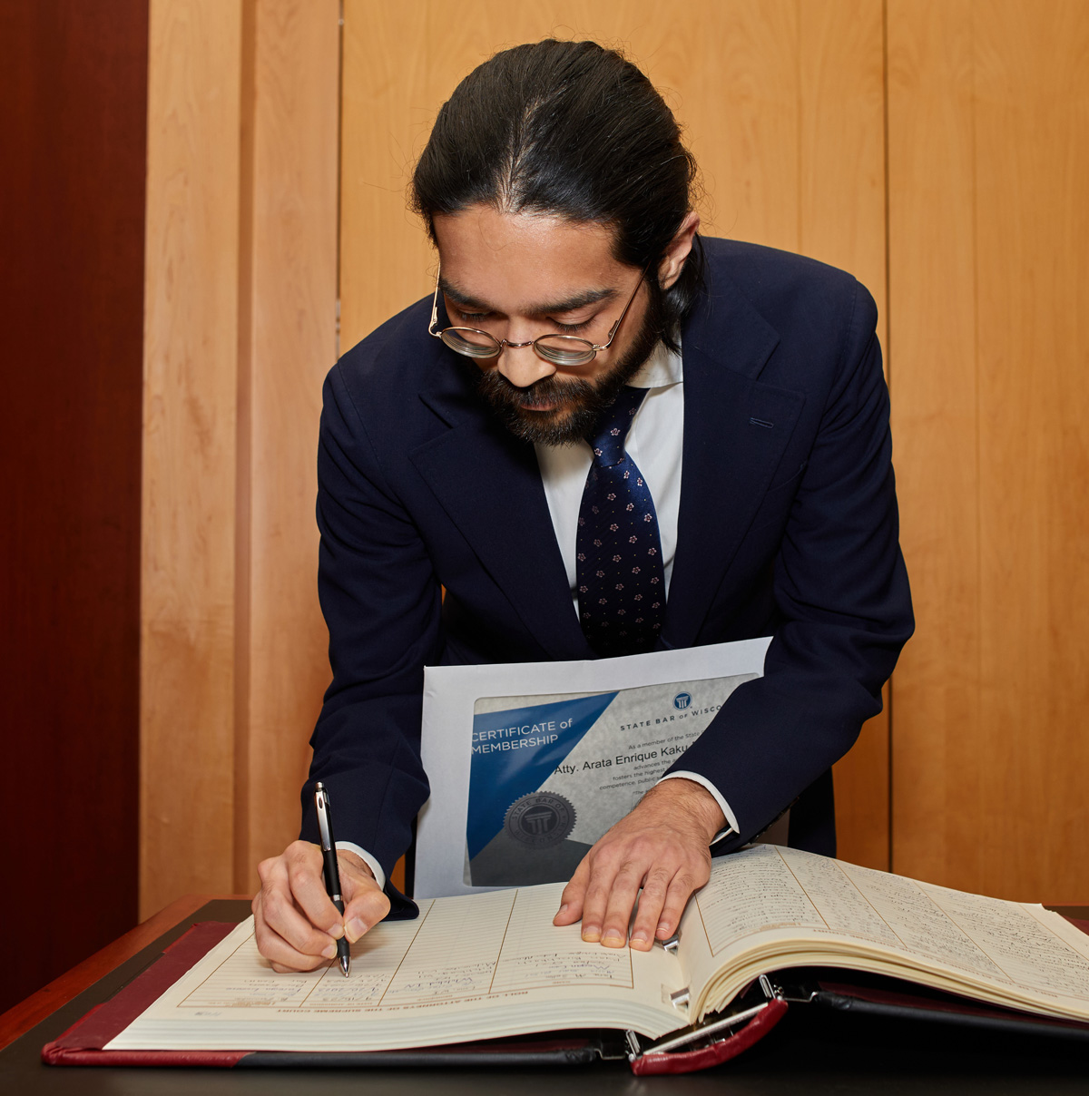 a man is bent over a book, signing his name