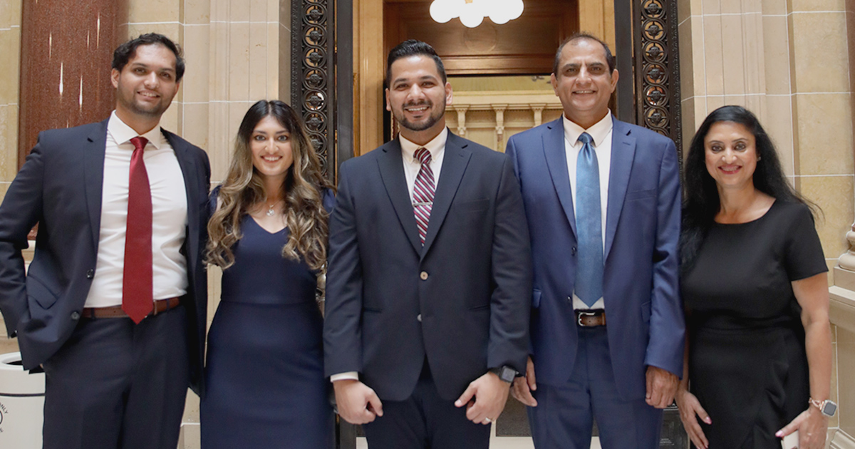 Five people stand and smile at the camera in front of the Wisconsin Supreme Court Hearing Room