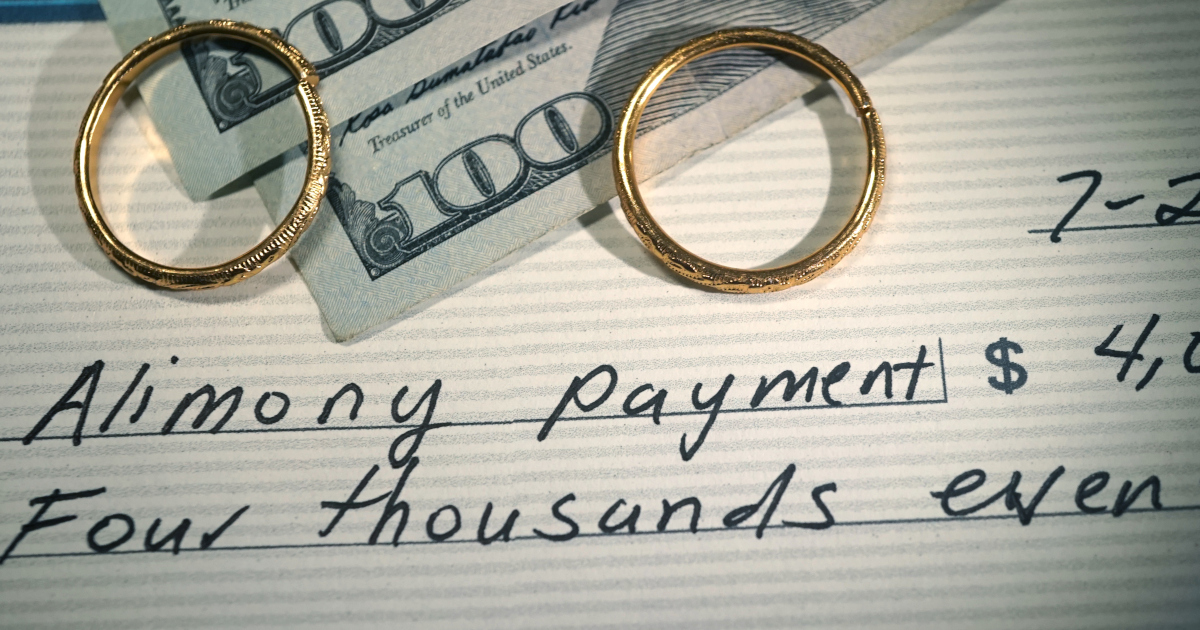 Two Gold Wedding Bands Lying Atop A Check Made Out To Alimony Payment, And Two Hundred Dollar Bills Lying On The Check