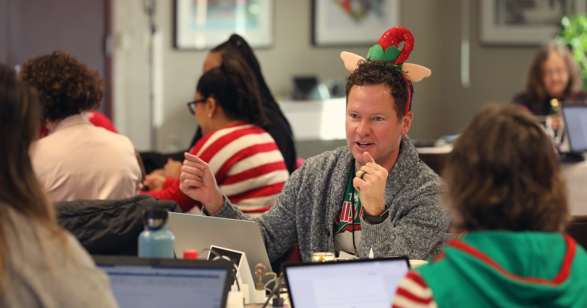 Erik Guenther wearing holiday attire and talking while sitting at a table