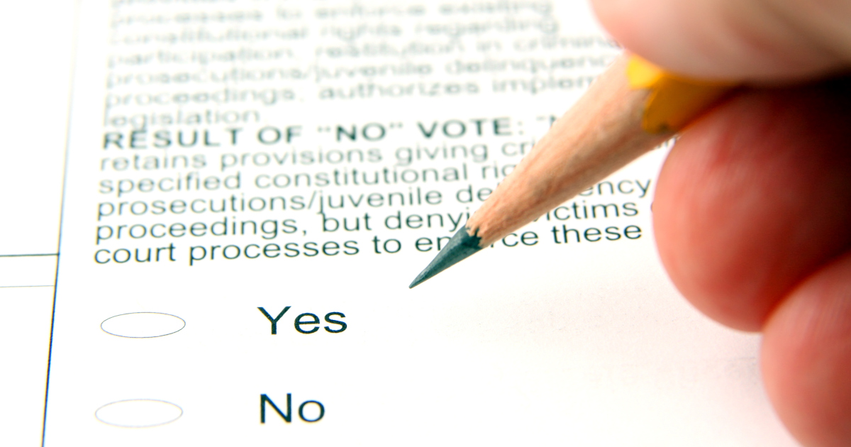 Closeup Of A Fingertips Gripping A Sharpened Pencil, Poised Over A BalLot That Reads In Part Result Of A No Vote