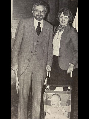 two adults smiling at the camera with a small child in a baby stroller