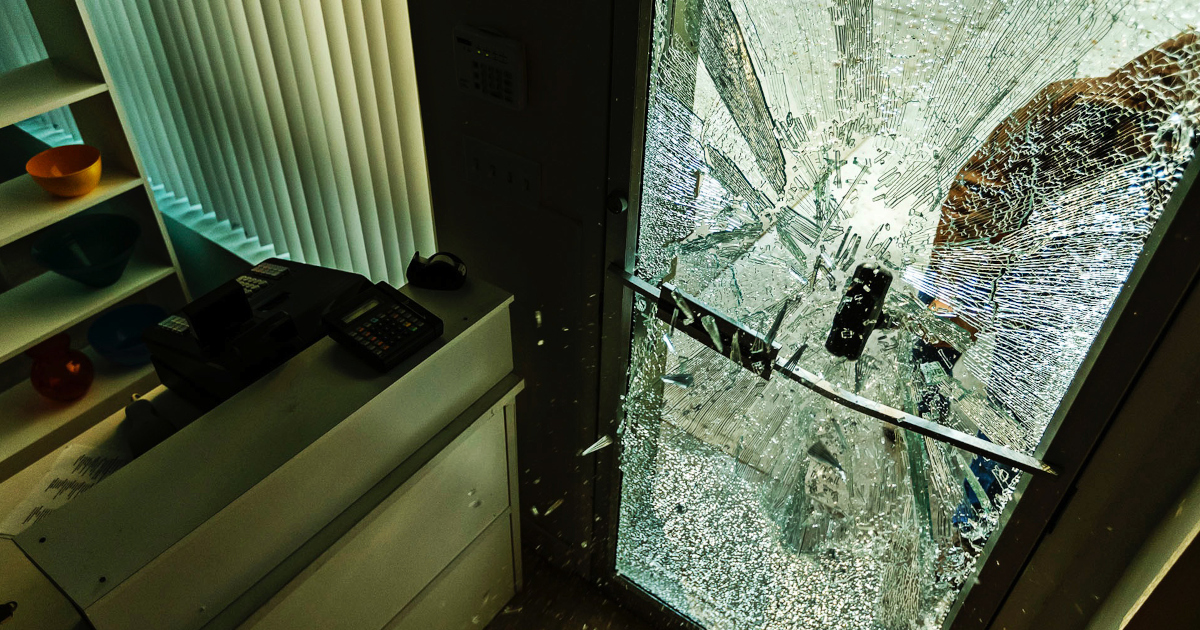 Close Up Wide View From Inside A Office As Someone Smashes A Sledgehammer Through A Glass Door On An Overcast Day