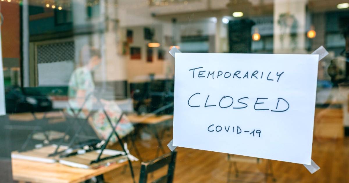 A Hand-Lettered Sign That Reads Temporarily Closed Covid-19 Hangs In A Shop Window
