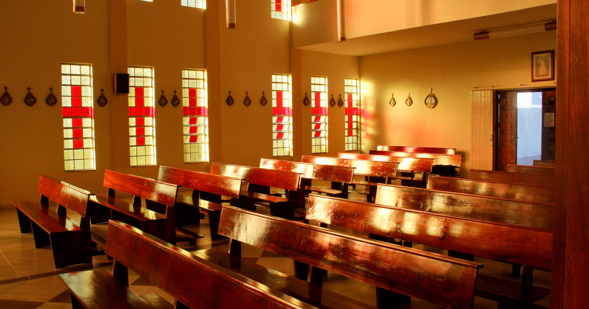 Sun Streaming Through Vertical Stained Glass Windows With Red Crosses, Illuminating A Sanctuary Of Plain Wooden Pews