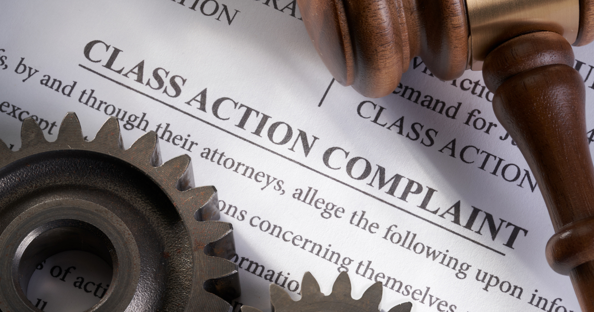 A Judge's Gavel Lying At An Angle On A Document That Reads Across The Top Class Action Complaint, With Two Iron Cogs Lying Across The Document Below The Gavel