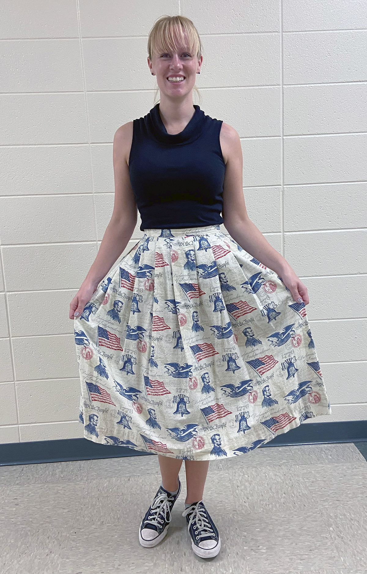 Lodi High School teacher Kelsie Barlow smiles at the camera and shows her pleated skirt made of fabric with U.S. flags, Abraham Lincoln, the Liberty Bell, an eagle, and the words We the People