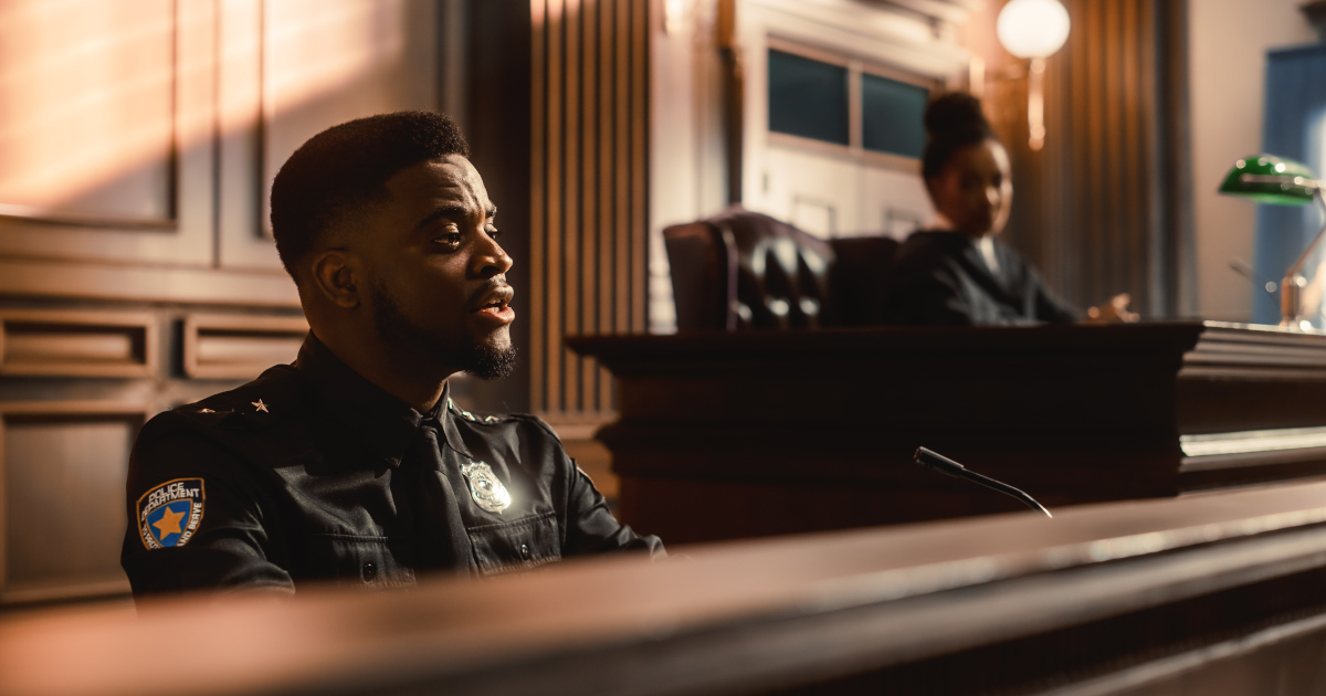 A Policeman In Uniform Testifying In A Courtroom Panelled With Dark Wood