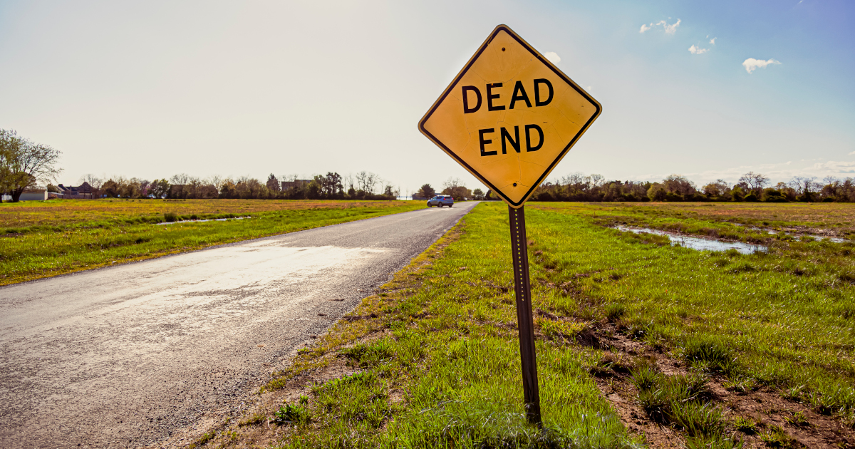 A Dead End Sign On Undeveloped Land Alongside A Road