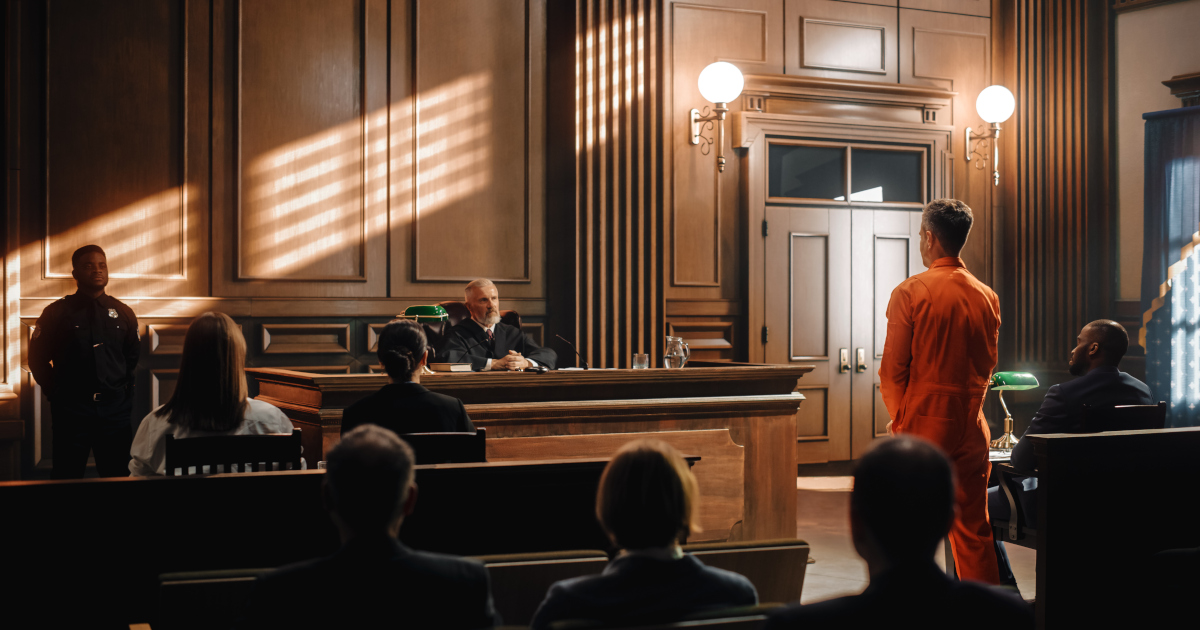 A Criminal Defendant In An Orange Jumpsuit Standing Before A Judge