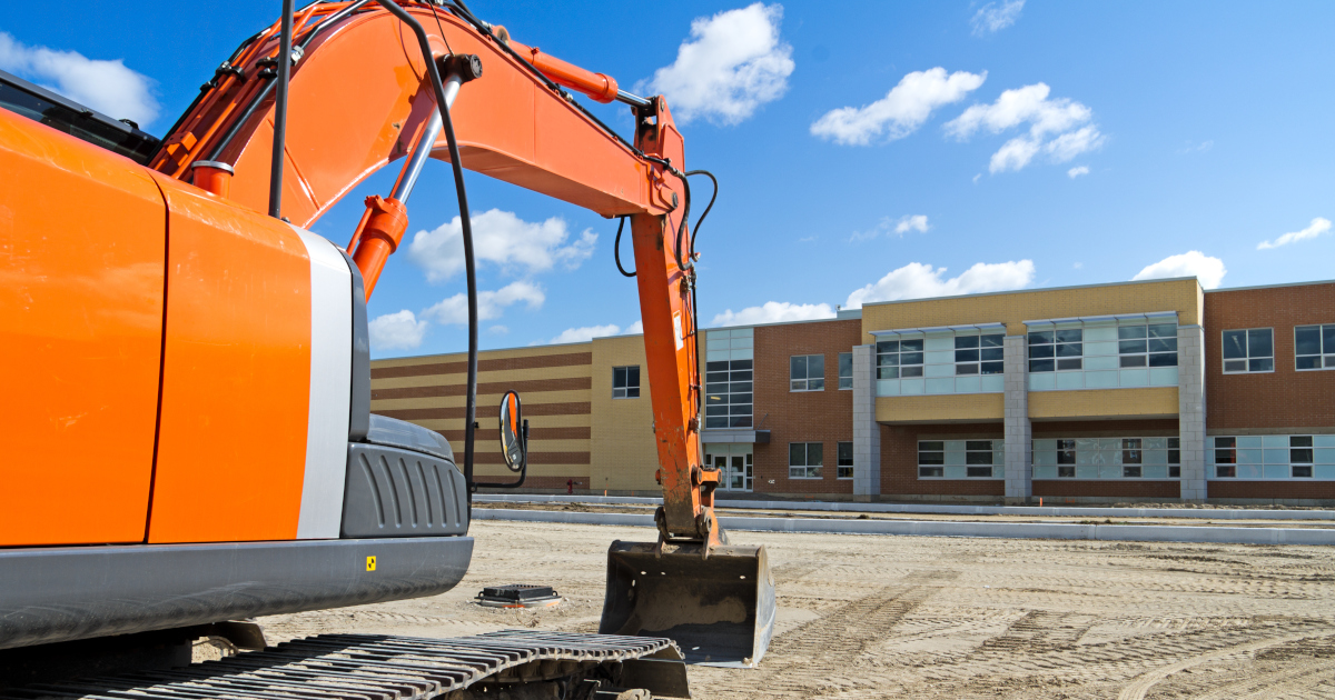 An Excavator Sits Idle Atop A Leveled Gravel Plain In Front of A New Building
