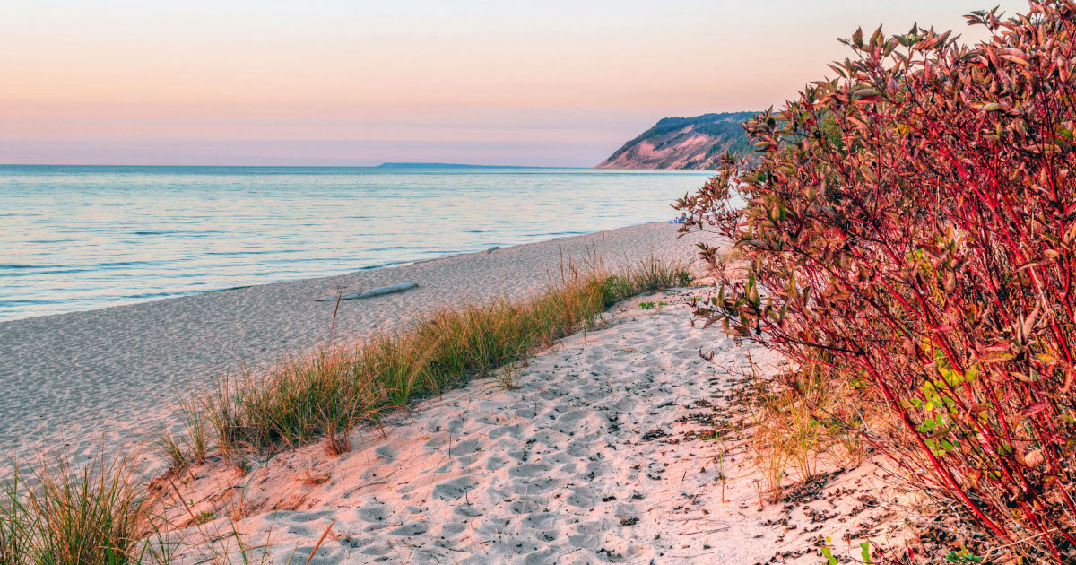 A Stretch Of The Lake Michigan Shoreline, With A Sloping Sand Beach In the Foreground, At Sunset