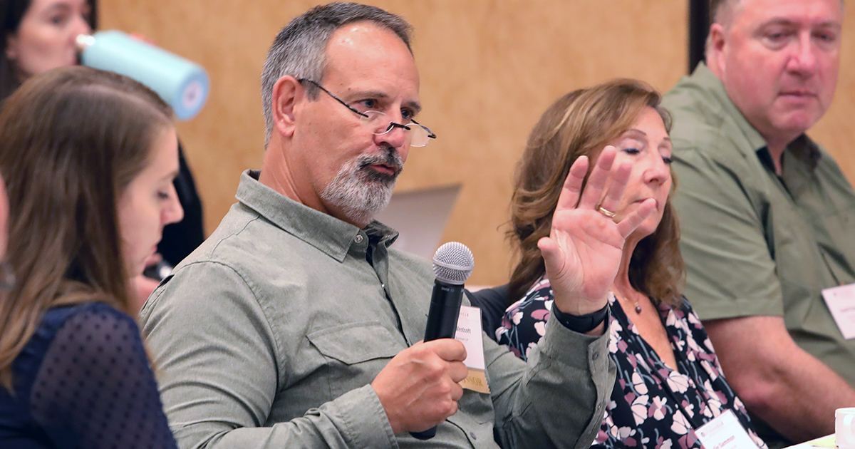 A Man Holding A Microphone Speaks While Gesturing With One Hand