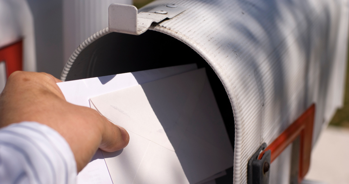 A White Man's Hand Placing A White Letter Enveloper In A Metal Mail Box Painted White