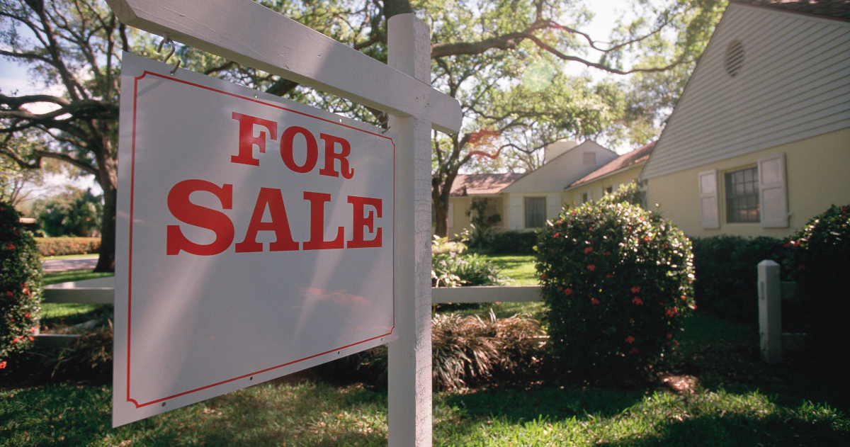 A Red And White For Sale Sign Outside A Cape Cod Style House Shaded By Trees On A Summer Day