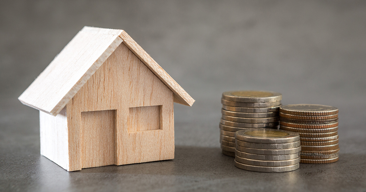 stock photo of toy-size wood house with a pile of coins