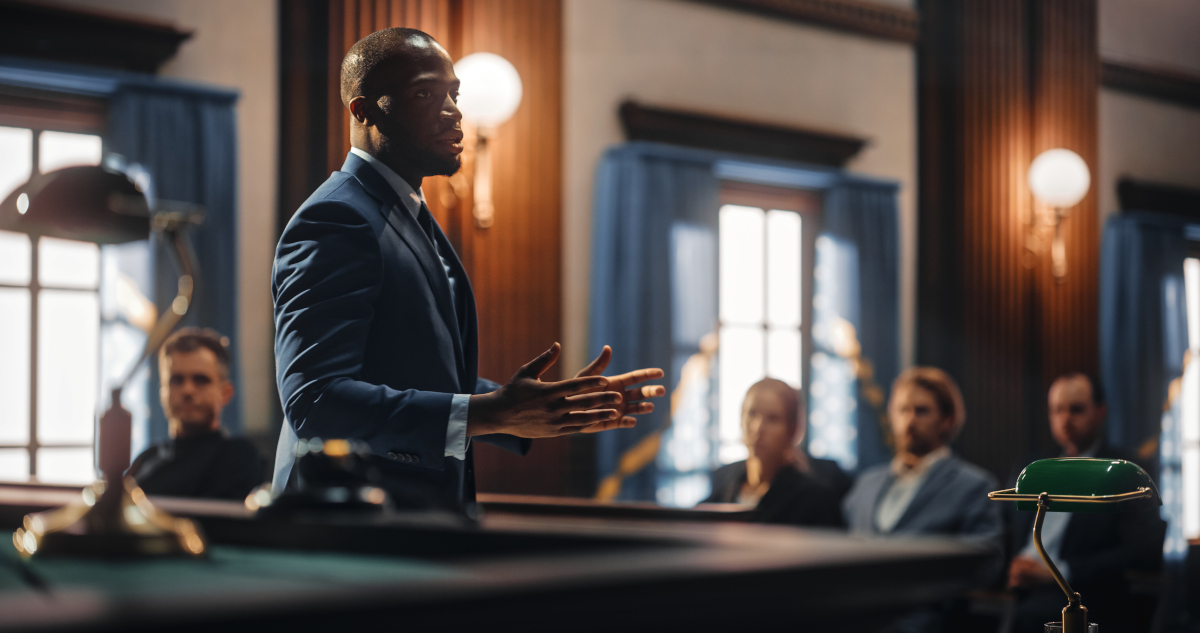 An Attorney In A Dark Suit Gesturing With Both Hands Open And His Arms Held Waist High, Arguing To The Jury