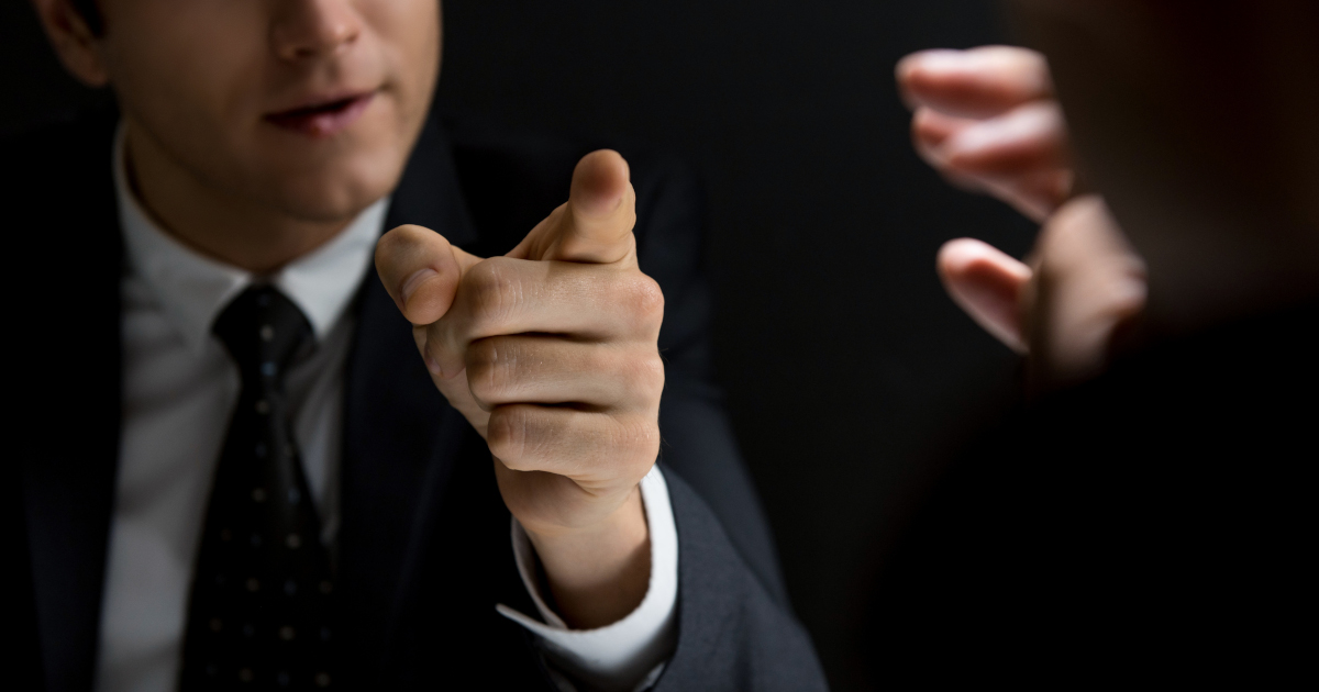 Across A Rectangular Wooden Table Two Lawyers, Each Dressed In A Black Suit, Argue And Gesture With Their Arms and Hands