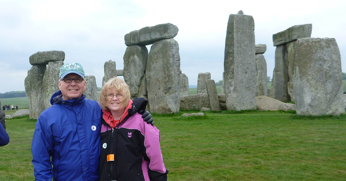 two people smile at the camera with Stonehenge in the background