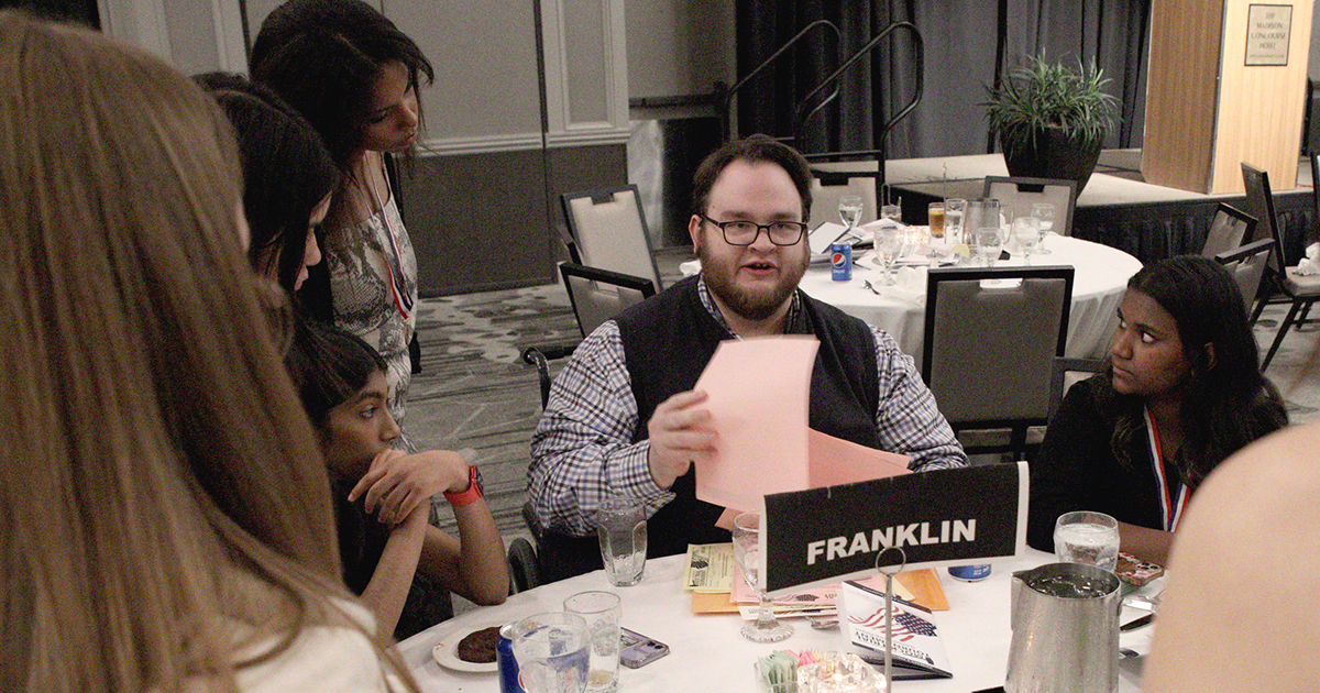 Teacher-coach Sam Koenig at a banquet table speaks with students