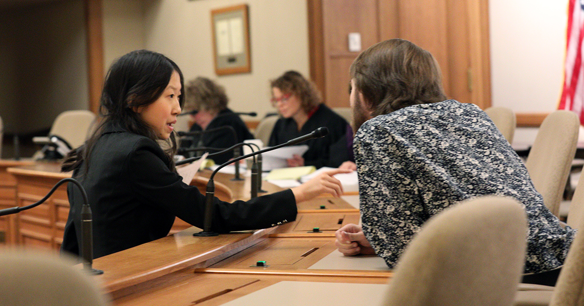 Alexis Hu points at the witness, who is seated at the witness table