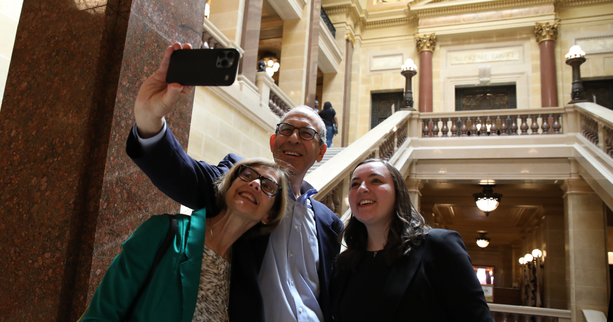 three smiling adults pose for a cell phone photo