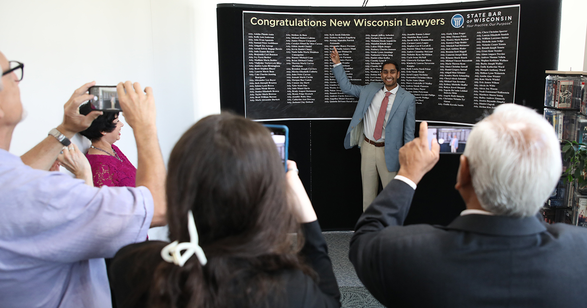 A smiling young man points to his name on a long list of names