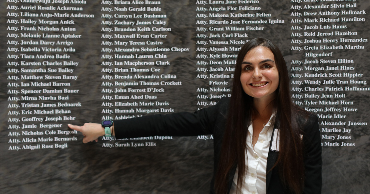 A woman smiles at the camera while pointing to her name on a list behind her