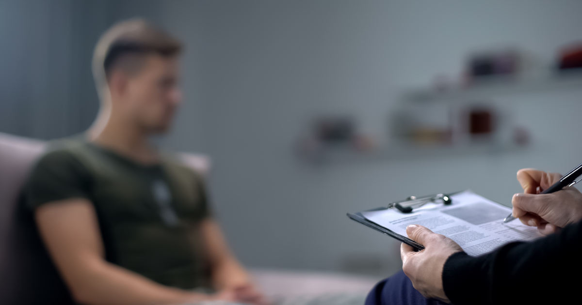 Out Of Focus Man Looking Away As A Doctor Makes Notes On A Clipboard